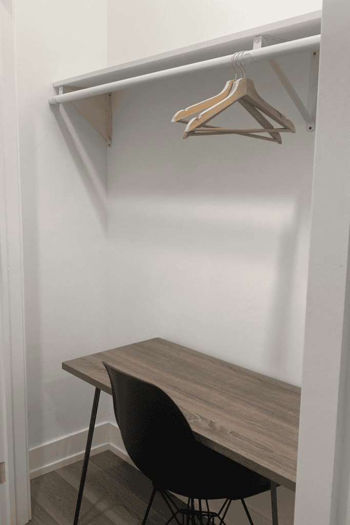 Small, minimalist home office with a wooden desk and black chair in a closet space.