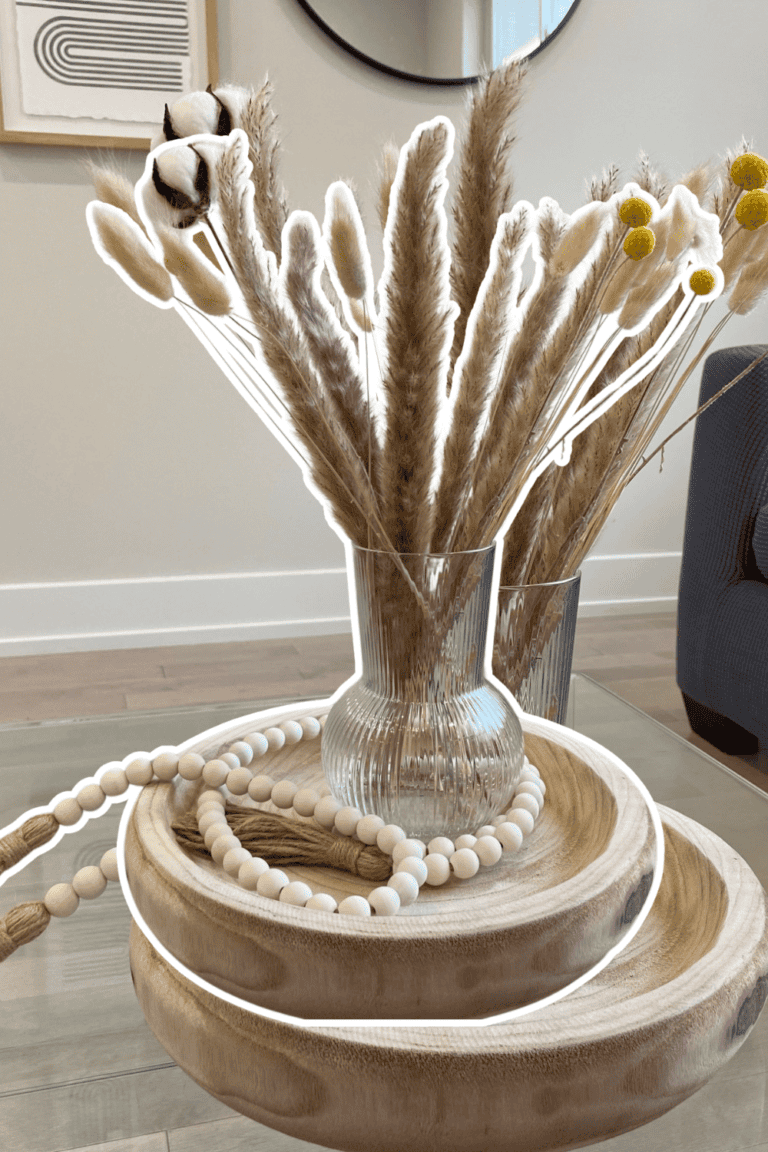 Elegant home decor featuring pampas grass in a glass vase with wooden accents and beaded accessories.