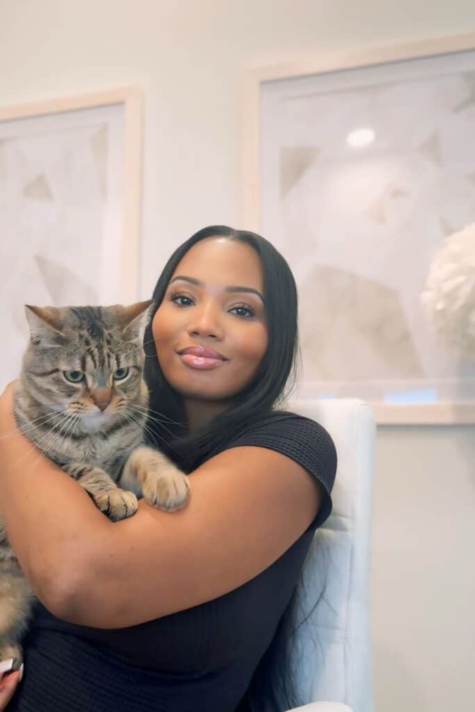 Woman embracing a tabby cat in a cozy, modern interior with soft lighting and elegant decor.